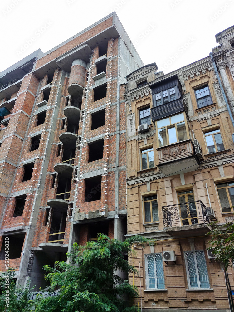 Two houses of different eras. One is under construction, the other is ancient. They stand next to each other Two houses of different eras. One is under construction, the other is ancient. They stand next to each other