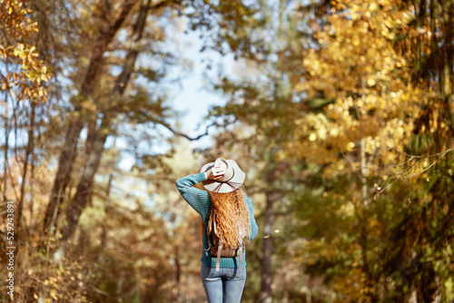 A young red-haired woman walks through the autumn park. A girl in a beige hat looks at the autumn forest
