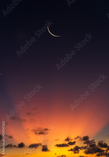 Crescent moon on dusk sky twilight vertical with orange sunlight after sundown