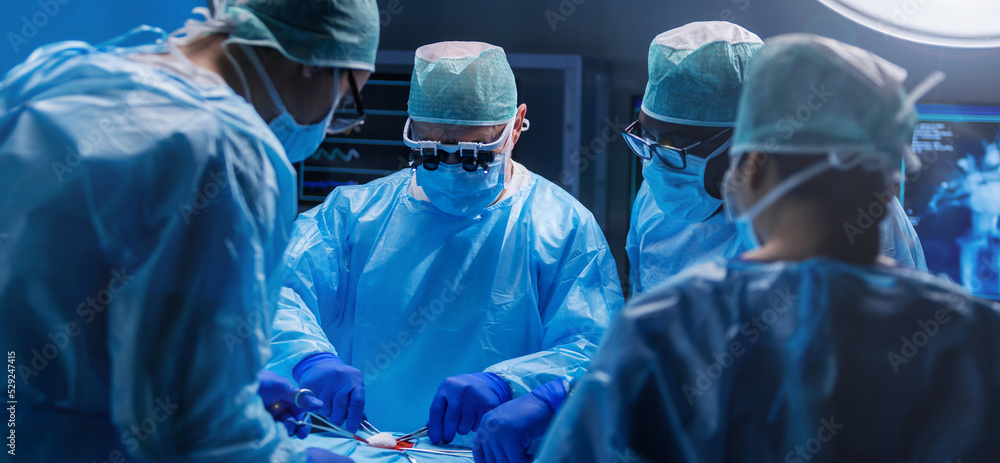 Diverse team of professional medical surgeons perform surgery in the operating room using high-tech equipment. Doctors work to save a patient in a modern hospital. Medicine, technology and healthcare. Diverse team of professional medical surgeons perform surgery in the operating room using high-tech equipment. Doctors work to save a patient in a modern hospital. Medicine, technology and healthcare.