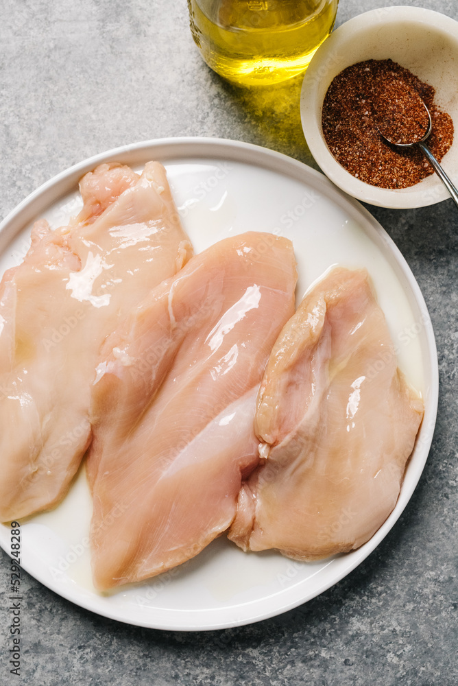 Oil drenched raw chicken breasts with a side of spice mix Oil drenched raw chicken breasts with a side of spice mix