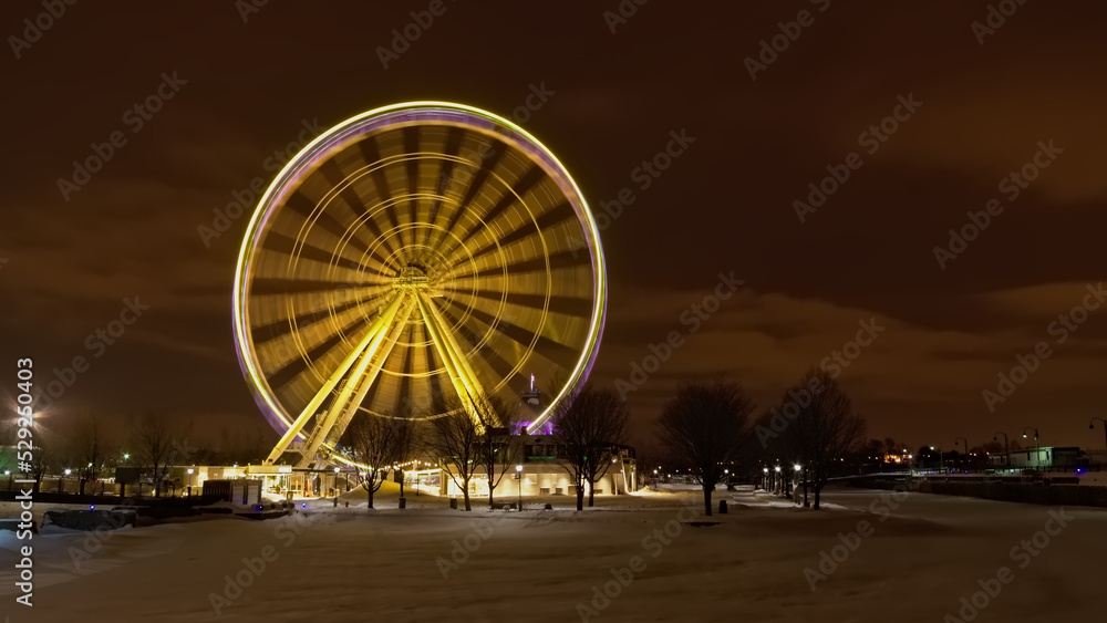 Illuminated ferris wheel at night on a cold winter day with snow on the ground in the Old Port of Montreal, Quebec, Canada. Long exposure with motion blur