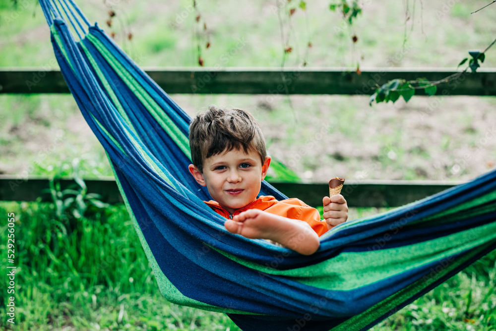 Little boy with ice-cream in hammock in village outdoor Little boy with ice-cream in hammock in village outdoor