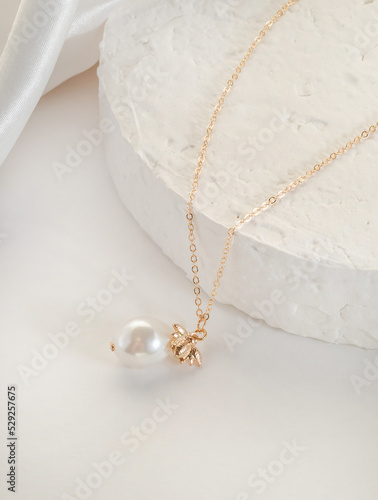 Photos Fashion bijouterie - a thin gold chain with a pendant and a bead on a white stan