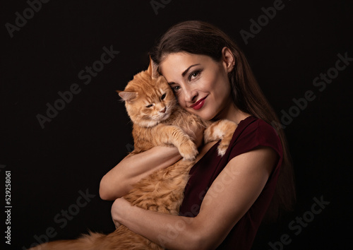 Beautiful make-up woman with brown long hair holding and tender hugging with love her red maine coon kitten. Closeup toned vintage color portrait.