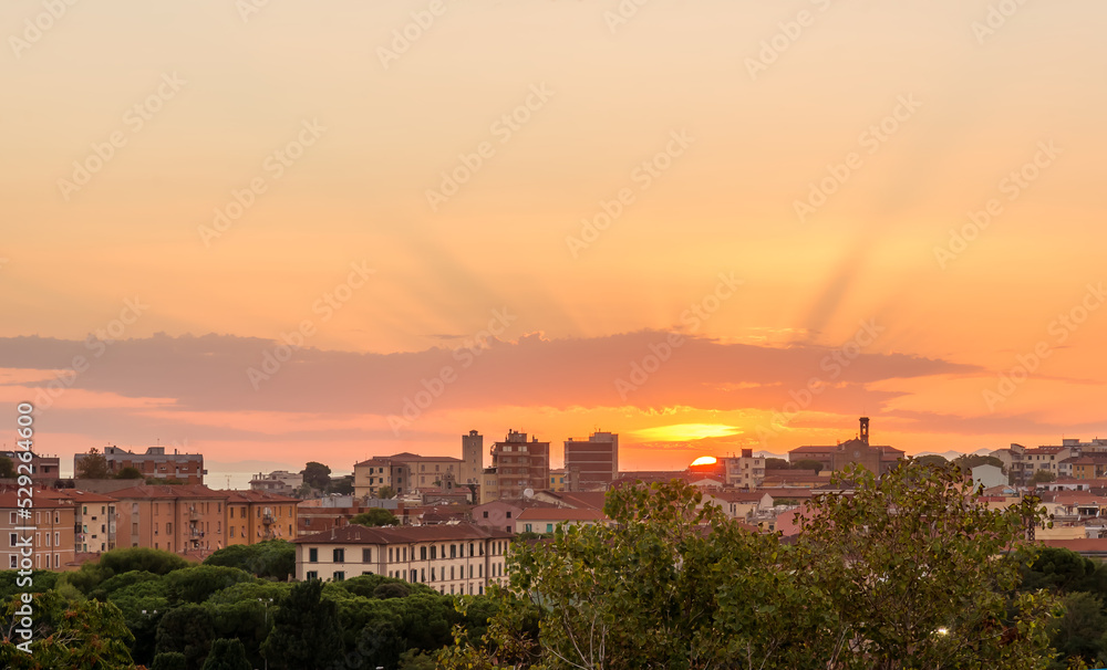 Gorgeous orange-lilac sunset over the city of Piombino, Tuscany, Italy. The rays of the sun pass through the clouds.