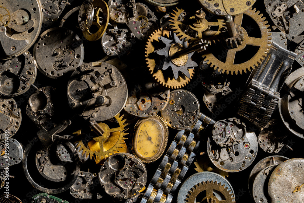 Top view of heap of metal internal parts of old clock. Dial, clockwork, bracelet, gears, cogwheels on black studio background. Disassembled clock mechanism of an old clock. Workshop, repair. Close up.