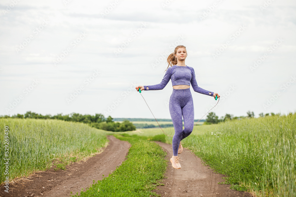 Young blonde woman doing exercises with a skipping rope on a country road Young blonde woman doing exercises with a skipping rope on a country road