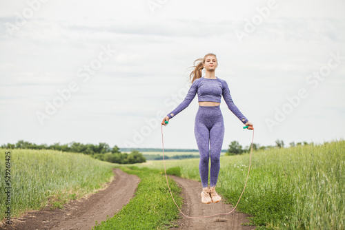 Young blonde woman doing exercises with a skipping rope on a country road