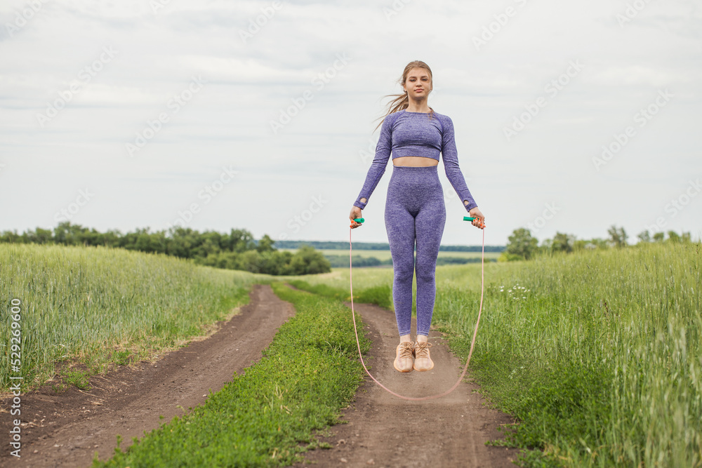 Young blonde woman doing exercises with a skipping rope on a country road Young blonde woman doing exercises with a skipping rope on a country road