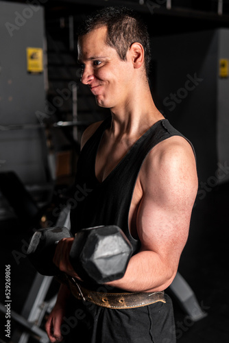 High quality photography. Man training in a gym. Caucasian man with a dark background lifting a dumbbell making a lot of effort. Man training arms with dumbbells.