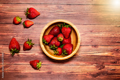 Strawberries in a wooden bowl on wooden table. Top view with space for text and flare effect.