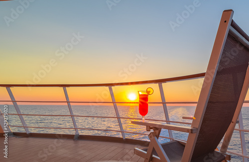 Papier peint Vue d'une chaise longue avec un cocktail sur le pont d'un navire de croisière au coucher de soleil dans le sillage du navire de croisière