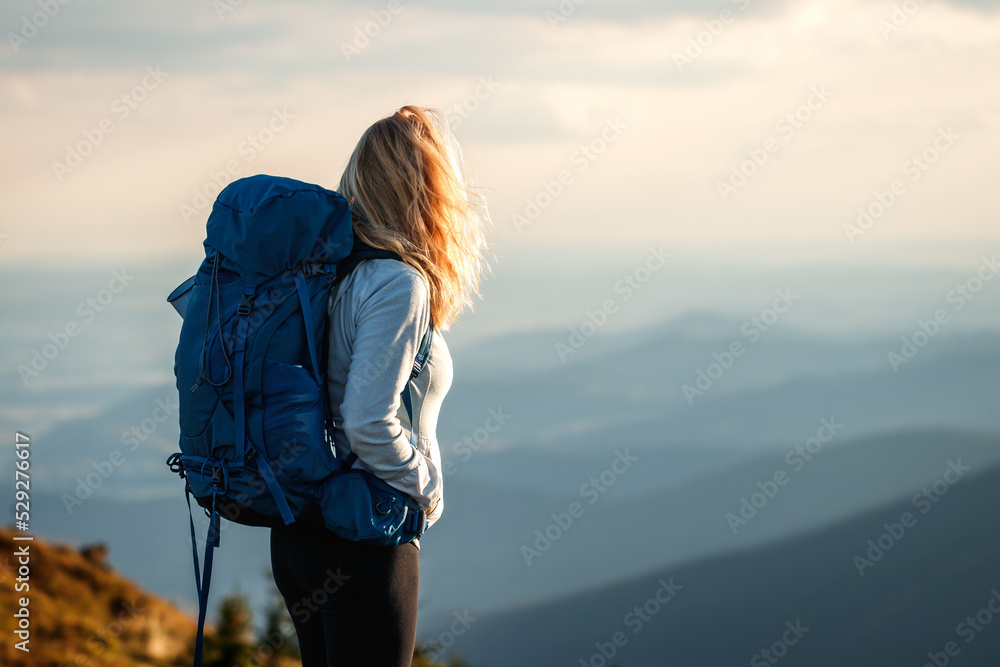 Woman with backpack trekking in mountains. Traveler hiking in nature