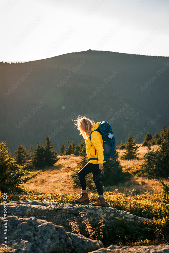 Woman with backpack hiking on mountain trail during sunset at autumn
