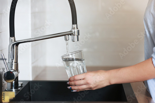 Woman filling drinking glass with tap water on the kitchen. Concept of clean drinking tap water at home. Pouring fresh drink. Water quality check concept. The concept of saving, problems with water