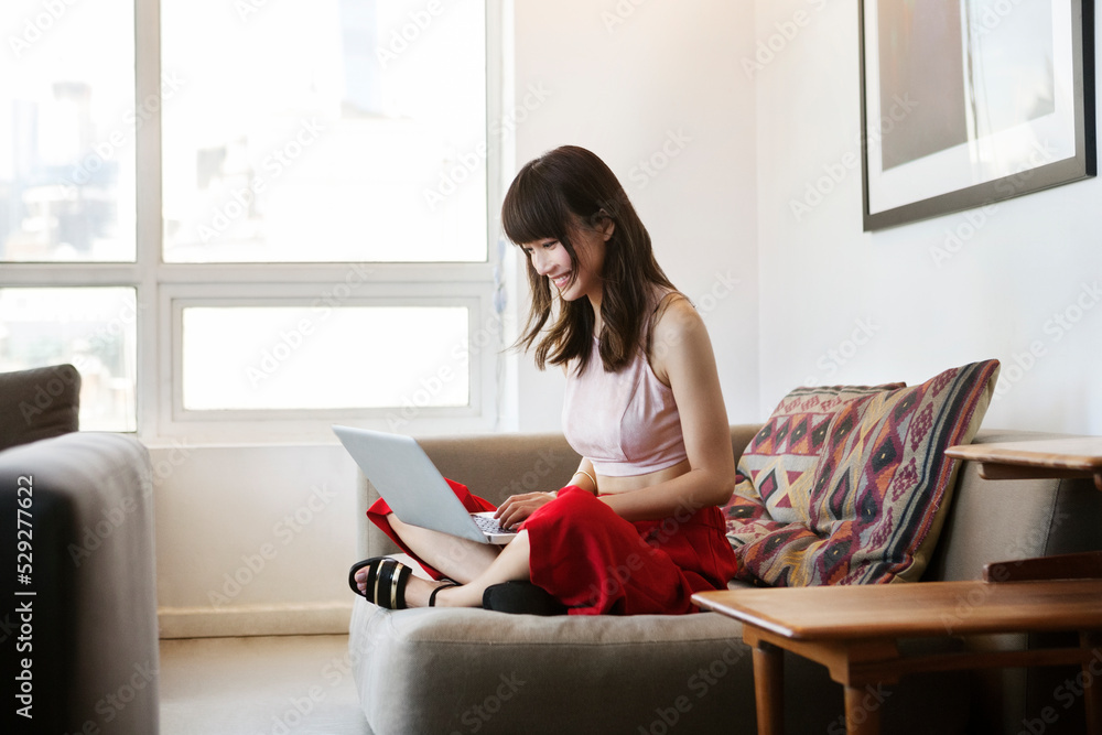 Smiling woman using laptop while sitting on sofa in office Smiling woman using laptop while sitting on sofa in office