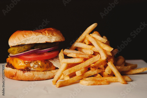 Close-up of hamburger with French fries on table against black background