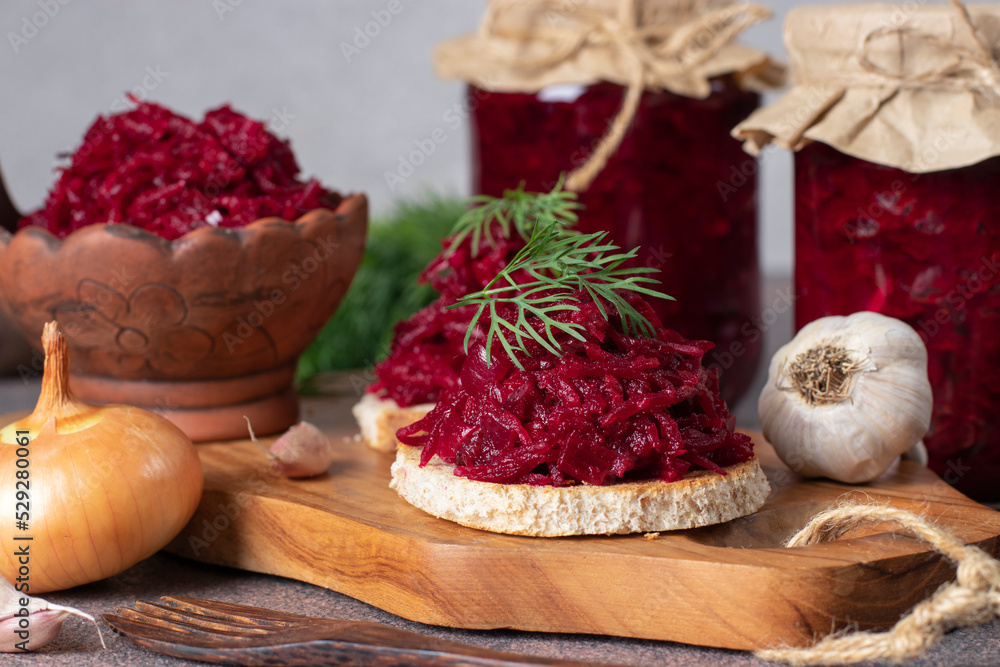 Homemade spicy caviar from beets, carrots, onions and garlic on toasted bread and also in jars on wooden board on light gray background Homemade spicy caviar from beets, carrots, onions and garlic on toasted bread and also in jars on wooden board on light gray background