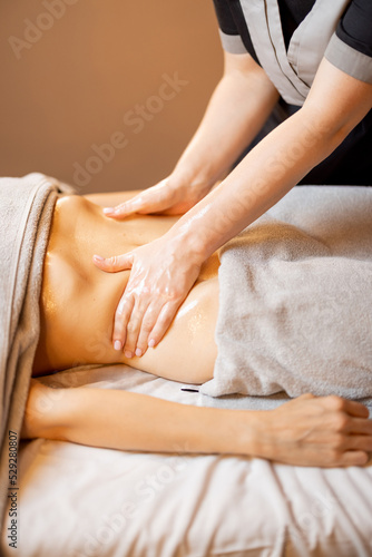 Masseuse performs professional abdominal massage for female client lying on a couch  close-up on hands