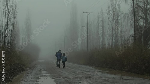 A Man and his Daughter Walking on a Rural Road in the Morning Fog in Varvarco, Neuquen Province, Argentina. photo