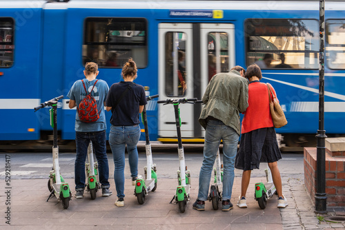 Four people are going to use an electric scooter in the city, a city tram passes by, activation of electric scooters, scooter rental in Krakow, eco-friendly transport