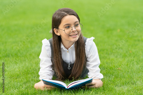 Portrait of happy teen girl reading school book lying on grass, education. School and education