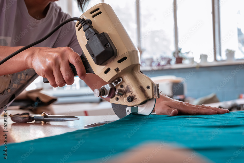 The cutter cuts the fabric with a disc knife in a sewing workshop The cutter cuts the fabric with a disc knife in a sewing workshop