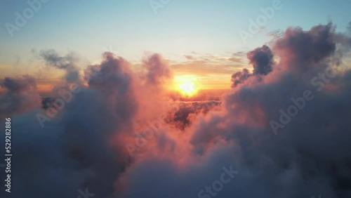 Moving white clouds blue sky scenic aerial view. Drone flies high back in blue sky through the fluffy clouds in the evening at the bright sun. Sun is hidden behind the clouds at sunset the fog. Nature