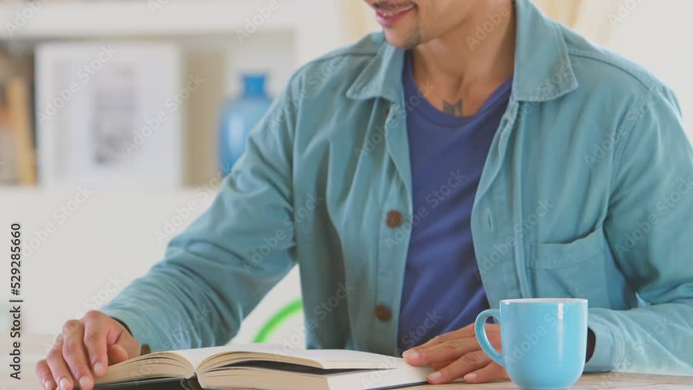 Man relaxing at home sitting at table reading book with hot drink - shot in slow motion Man relaxing at home sitting at table reading book with hot drink - shot in slow motion