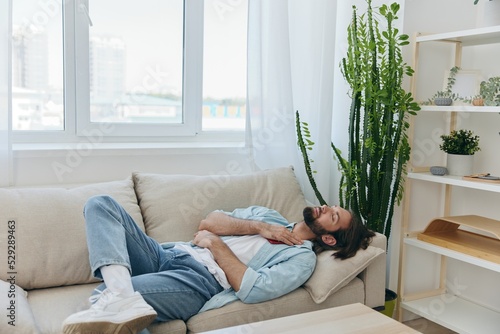A man with a beard sleeps on the couch in the afternoon tired and relaxed after stress and ill health. Stress at work, poor sleep and health problems