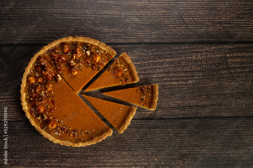 A pumpkin pie with a single slice separated, set against a dark wooden table, embodying the essence of autumn indulgence A pumpkin pie with a single slice separated, set against a dark wooden table, embodying the essence of autumn indulgence