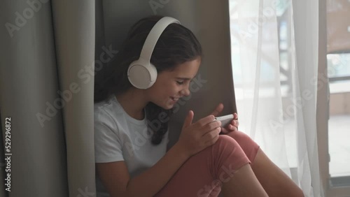 Girl of 10 years communicates with friends via video call. Teens wins a game on the phone at the desk at home in the living room. Happy adult child listens to music, plays games, studies with lessons photo