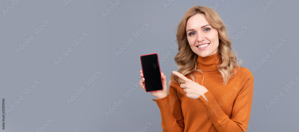 Naklejka premium Happy girl pointing finger at mobile phone. Pointing index finger for advertising. Woman portrait, isolated header banner with copy space.