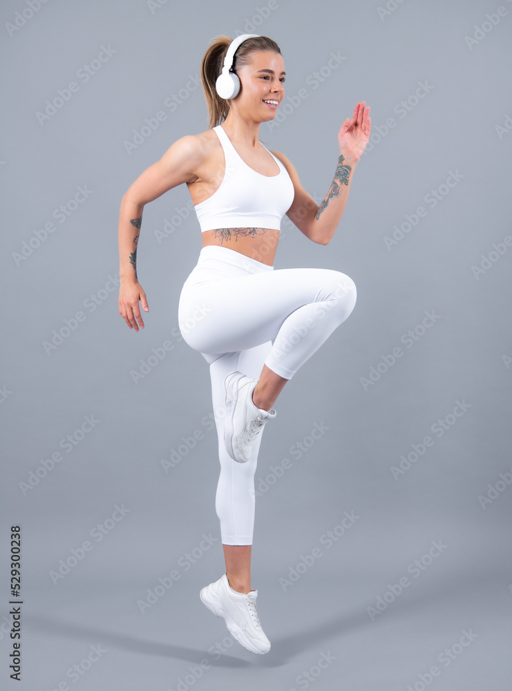Young fitness woman runner with headphone run on gray background. Dynamic movement. Sport and healthy lifestyle. Young fit woman. Healthy lifestyle and sports concept. Isolated on gray. Young fitness woman runner with headphone run on gray background. Dynamic movement. Sport and healthy lifestyle. Young fit woman. Healthy lifestyle and sports concept. Isolated on gray.