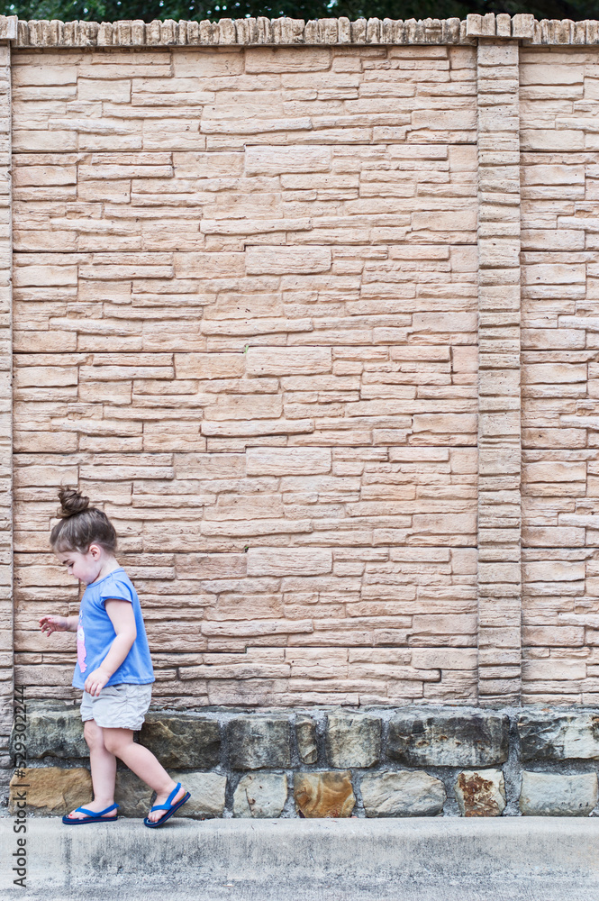 Side view of girl walking on footpath against wall Side view of girl walking on footpath against wall