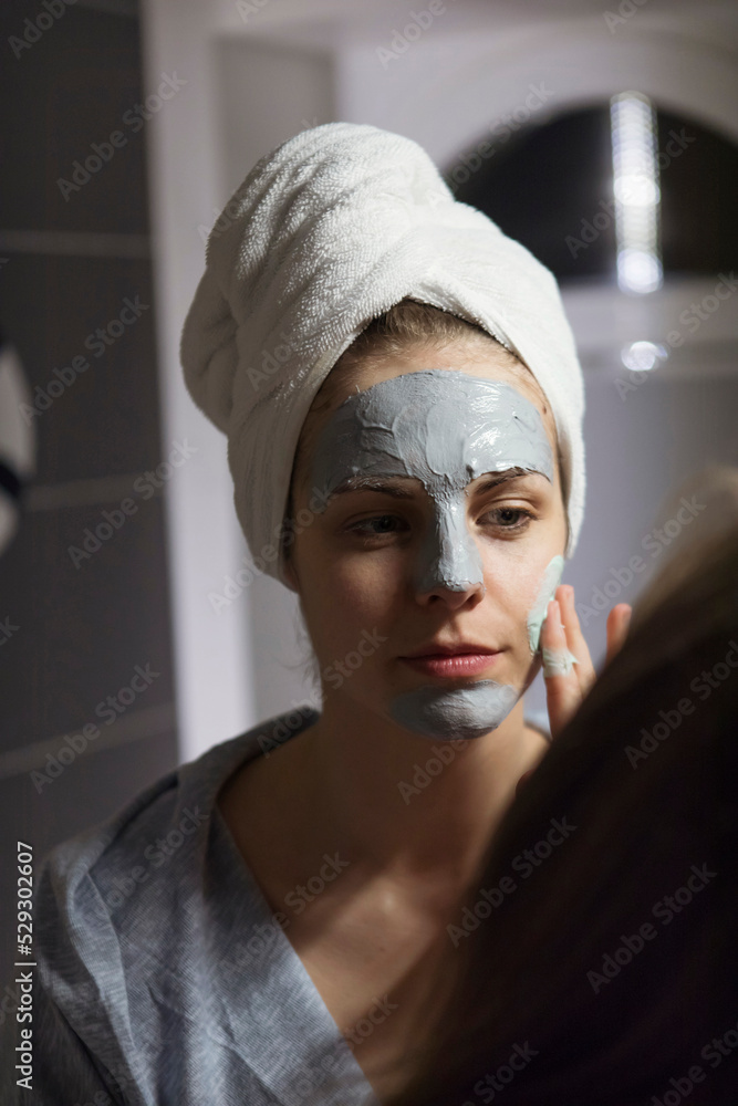 Reflection of woman applying facial mask in mirror at bathroom Reflection of woman applying facial mask in mirror at bathroom