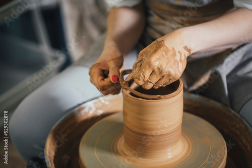 Midsection of female potter cutting clay on pottery wheel with thread at workshop photo