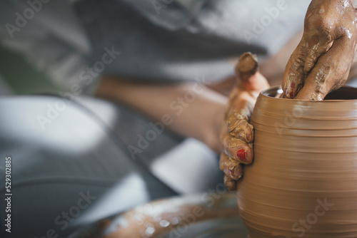Midsection of female potter shaping clay on spinning wheel at workshop