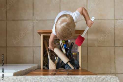 Overhead view of baby boy removing kitchen utensils from drawer photo