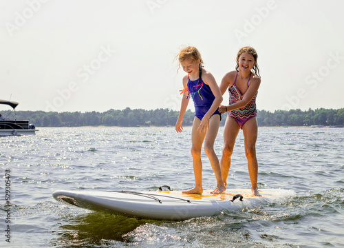 Cheerful siblings standing on paddleboard in lake against clear sky during sunny day photo