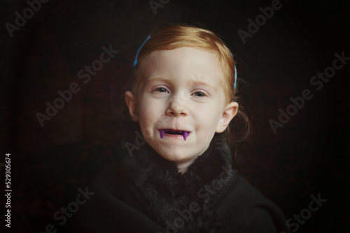 Close-up portrait of girl with vampire teeth standing against black background photo