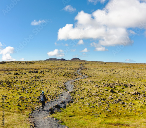 High angle view of hiker walking on trail amidst field against cloudy sky photo