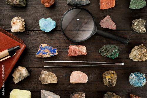 Overhead view of colorful gemstones with magnifying glass and tweezers on wooden table photo