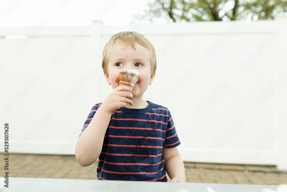 Boy eating ice cream cone while sitting at table against wall Boy eating ice cream cone while sitting at table against wall