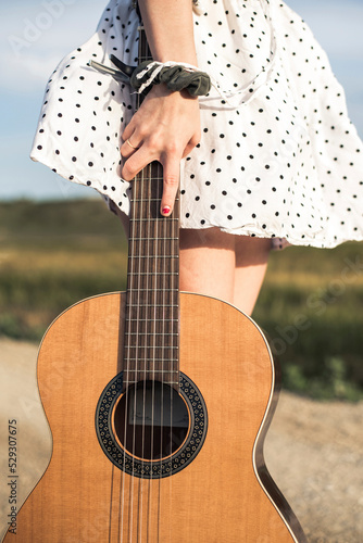 Midsection of woman holding guitar while standing on field against sky