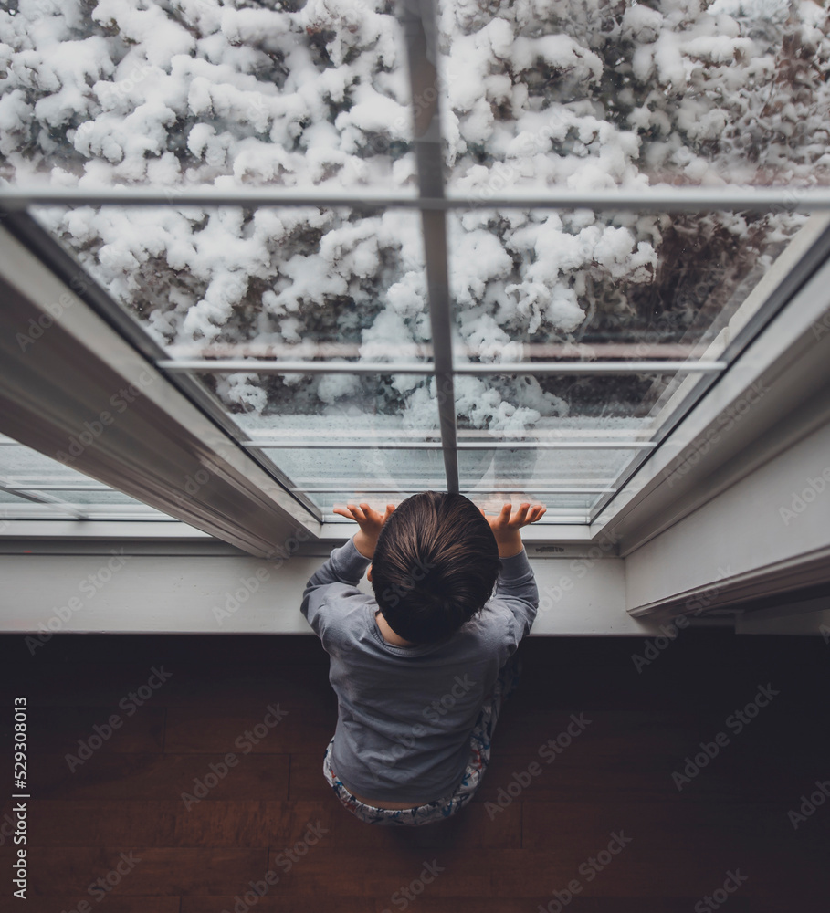 High angle view of boy looking through window at home during winter High angle view of boy looking through window at home during winter