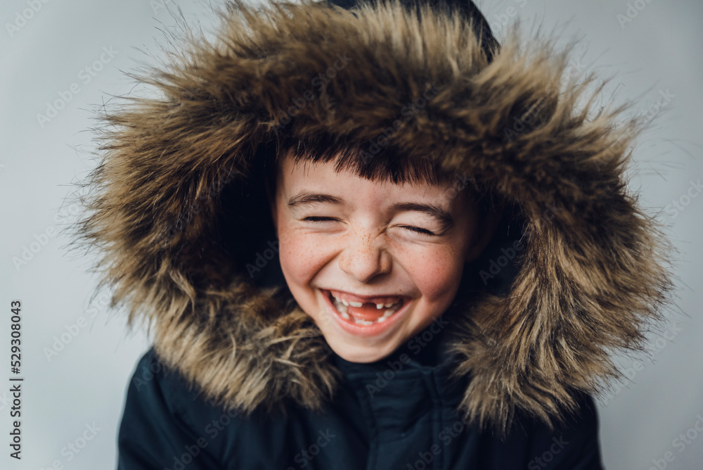 Close-up of happy boy in fur coat standing against white background Close-up of happy boy in fur coat standing against white background