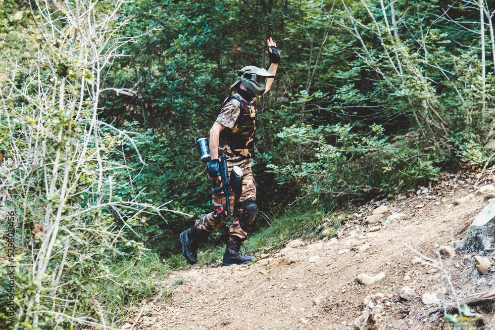 Side view of army solider with gun waving hand while walking on hill in forest Side view of army solider with gun waving hand while walking on hill in forest