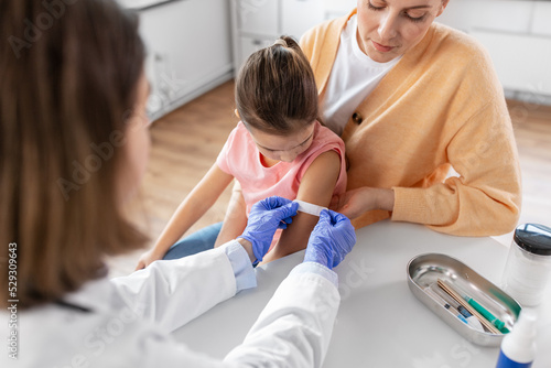 medicine  healthcare and pediatry concept - female doctor or pediatrician attaching medicinal patch to arm of little girl patient with mother at clinic